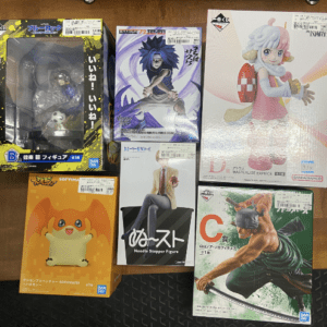 Six boxed anime and game figures laid on a wooden floor; includes characters from various series in colorful packaging.