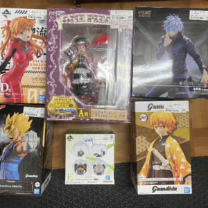 Collection of boxed anime figures arranged on a wooden floor, including characters from Evangelion, Dragon Ball, and One Piece-themed boxes.