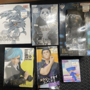 Six boxed anime figures arranged on a black patterned surface, including a blue-haired character and a panda figure among them.