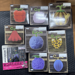 Assorted fruit-shaped novelty soaps or candles in decorative wooden-patterned boxes displayed on a dark mat.