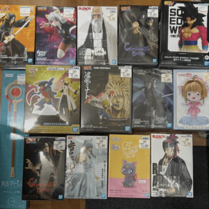 A grid of boxed anime figures on a wooden floor, featuring Naruto, Bleach, Dragon Ball, and other collectibles with price stickers visible.
