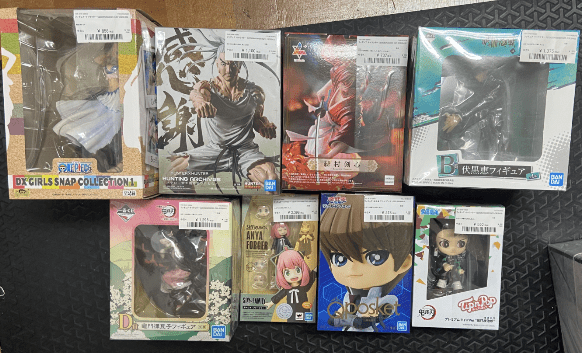 Captura De Pantalla 2026-04-28 a Las 164006 - Articulos Japan (post Box Japan) Assortment of boxed anime figures laid out on a dark floor mat, still in packaging with visible labels and artwork. Articulos Japan (Post Box Japan)