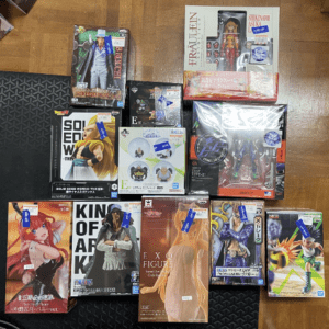 Assorted anime and collectible action figure boxes spread out on a wooden floor, featuring colorful packaging from various brands.