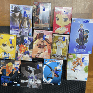 A collection of boxed anime action figures laid out on a wooden floor, featuring colorful character art (One Piece, Naruto, and friends).