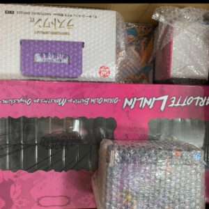 Open shipping box with bubble-wrapped toy boxes; a pink windowed box and a white box with a purple cartridge on top.