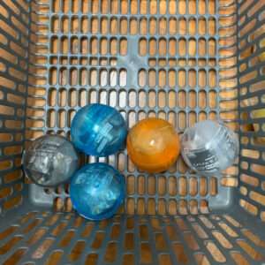 Five plastic capsule toys in a gray shopping basket: blue, orange, and clear capsules scattered on the grid interior