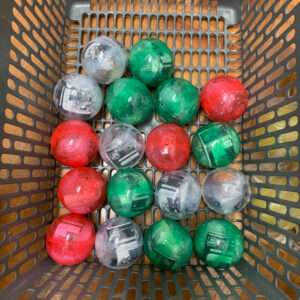 Plastic Christmas ornament balls in red, green, and silver inside a gray shopping basket.