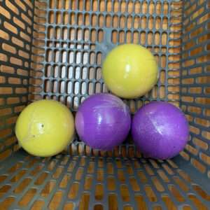 Four rubber balls—two yellow and two purple—in a gray plastic basket.
