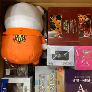 Large white plush with an orange outfit sits inside a box beside several anime figure boxes, including Evangelion merch.
