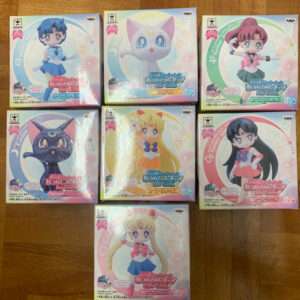 Six colorful boxed Sailor Moon figures on a wooden floor, each box showing a different character pose and outfit.