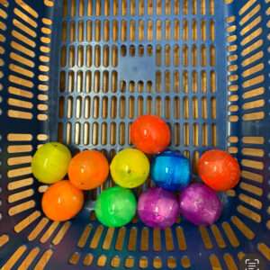 Colorful plastic balls in a blue perforated basket. The balls are bright orange, yellow, green, blue, and purple.