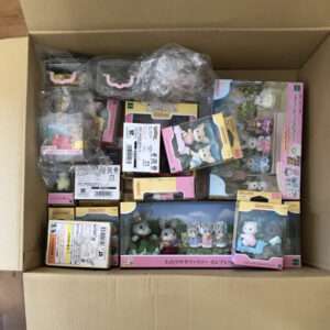 Opened cardboard box filled with numerous small animal figurine toys in colored packaging (pink, yellow, blue), some still in plastic bags.