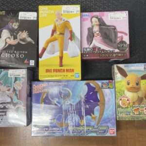 Six boxed anime figures displayed on a dark floor: Jujutsu Kaisen Choso, One Punch Man figure, Demon Slayer figure, a green-haired Flower character figurine, a Pokémon Eevee figure, and a large blue dragon Pokémon box.