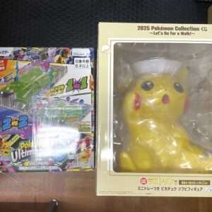 Two boxed Pokemon toys on a wooden floor: a colorful game/collector box on the left and a large yellow Pikachu figure inside a beige display box on the right.
