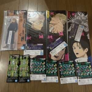 Collection of Japanese anime merchandise: three large poster boards with characters laid on a wooden floor, plus packaged figure and magnet/card sets laid out below.  Articulos Japan (Post Box Japan)