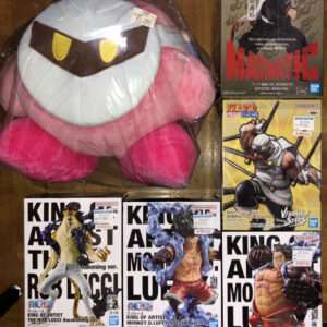Large pink plush character with a white face and brown eyes sits on a wooden floor next to boxed anime figures.
