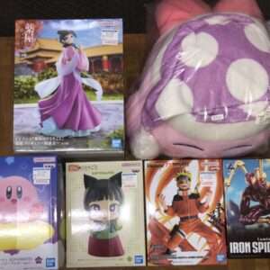Boxed anime figure of a woman in a pink kimono with a temple backdrop, top shelf beside a purple plush with white polka dots, all on a wooden shelf.