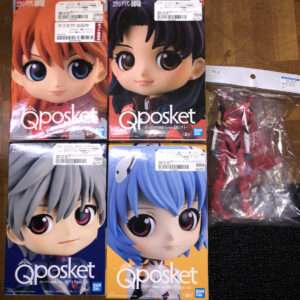 Four Qposket boxes with large anime-style faces: red-haired, black-haired, gray-haired, and blue-haired figures on a wooden floor, plus a red action figure in plastic bag on the right.  Articulos Japan (Post Box Japan)