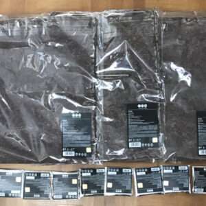 Large, vacuum-sealed black bags in plastic wrap laid on a wooden floor, with a row of small black boxes lined up in front.
