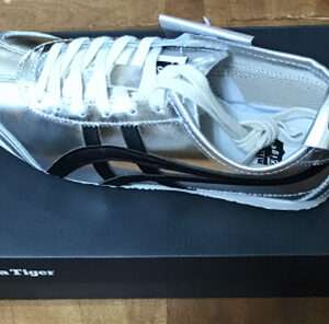 Metallic silver Onitsuka Tiger sneaker with white laces displayed atop a dark blue shoe box.
