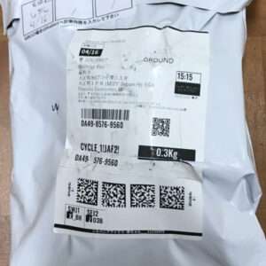 Padded grey shipping package with a white label showing tracking barcodes, QR codes, 'GROUND', 15:15, weight 0.3 kg, and a bright yellow SX1 sticker.