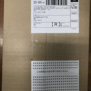 Cardboard shipping box with a white Japanese label showing a barcode and tracking numbers on the top panel; contains Japanese text and address lines.