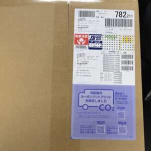 Cardboard box with a vertical shipping label showing barcodes, Japanese text, and a purple CO2 label.