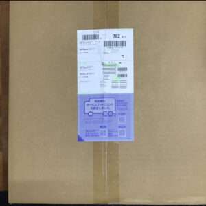 Brown cardboard parcel with central white shipping labels featuring barcodes and numbers, and a purple CO2 information label attached.