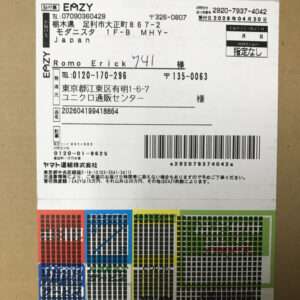 Shipping label on a brown box with Japanese text, recipient name Romo Erickk, phone numbers, a large barcode, and a colorful grid pattern at the bottom.
