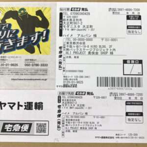 Close-up of a Japanese shipping label with barcodes and address blocks; left side features a bright yellow promotional graphic with a flexing superhero silhouette.