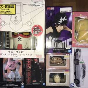 Display of collectible toy boxes on a store shelf, including a large Gundam head box and a purple Maximat figure and smaller character boxes.