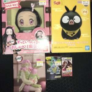 Two boxed anime figures on a store shelf: left box shows a pink package with a girl character with long black hair and pink eyes holding a bamboo gag; right box is yellow with a large black pig-like character wearing a yellow scarf.  Articulos Japan (Post Box Japan)