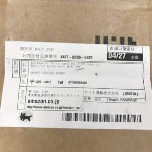 Shipping label pasted on a brown box showing sender/recipient details, barcodes, and a date like 2026年04月26日 (Japanese text). Includes Amazon.co.jp URL and shipment info.