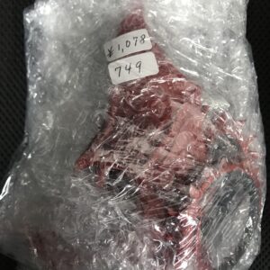 Red item wrapped tightly in clear plastic wrap with two price stickers showing ¥1,078 and 749.