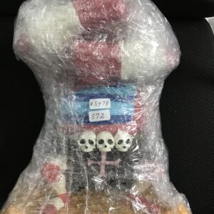 Plastic-wrapped skeleton toy with skulls along the torso, lying on a dark surface.