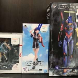 Shelf of anime figure boxes; a large Evangelion box on the right and a blue-skinned character box in the middle with a female figure on the left.