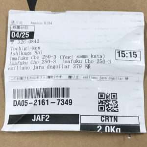 White shipping label on a cardboard box with multiple text lines, a barcode, a QR code, date 04/25, time 15:15, and weight 2.0 kg—describes delivery info and destination details.