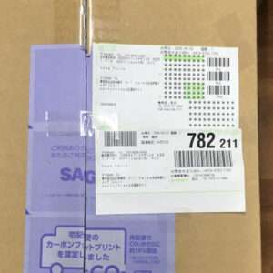 Brown cardboard package with a purple-taped side, featuring white shipping labels with barcodes and numbers on the front
