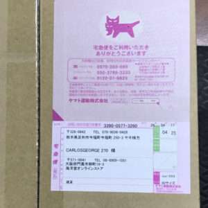 Shipping label on a brown cardboard box with a pink section, cat logo, and Japanese text outlining recipient address and details.