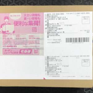 Brown cardboard parcel with two shipping labels: a pink label on the left featuring a cartoon courier, and a white label with a barcode on the right.