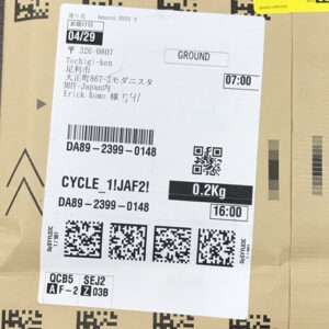 Shipping label on a cardboard box with 'GROUND', date 04/29, weight 0.2 kg, time 16:00, and multiple barcodes/QR codes visible.
