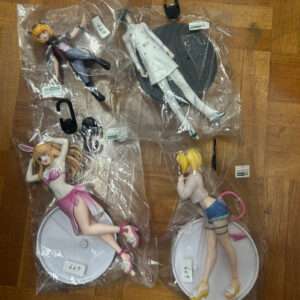 Assorted anime figurines sealed in plastic bags laid out on a wooden floor, each on a circular base.  Articulos Japan (Post Box Japan)