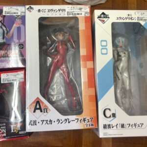 Five anime figure boxes on a wooden floor, including Evangelion figures and two large windowed boxes labeled A賞 (Asuka in red) and C賞 (Rei Ayanami in white).  Articulos Japan (Post Box Japan)