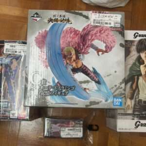 Three boxed anime figures arranged on a wooden floor: a large central figure with pink hair and a blue energy effect, flanked by two other Bandai Grandista boxes.