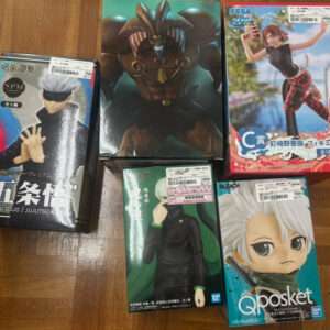 Collection of Japanese anime figure boxes arranged on a wooden floor, featuring Jujutsu Kaisen Satoru Gojo and Bleach Qposket figures, plus a SEGA figure box in the background.