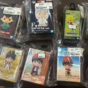Assorted anime chibi figurines in clear plastic packaging laid on a table, each with price tags visible on the packaging.