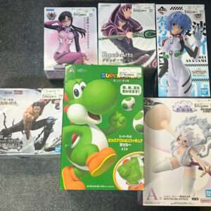 Pile of boxed anime figurines on a dark carpet, with a bright green Yoshi box in front and several character boxes behind it.