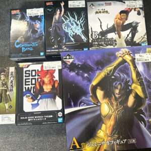 A collection of anime figure boxes on a dark floor, featuring characters from Naruto, Dragon Ball, and Saint Seiya boxes by Bandai/Bluefin.