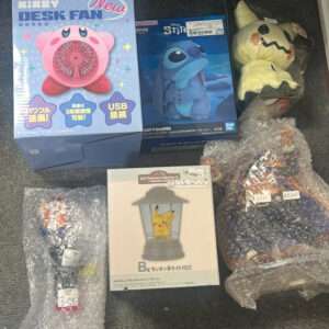 Various novelty items on the floor: a pink Kirby desk fan box, a Stitch figurine box, and yellow Pikachu lamp/lantern packaging with surrounding bubble-wrapped items.