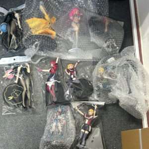 Collection of anime figurines in plastic bags and bubble wrap laid out on a gray carpeted floor, ready for packaging or display.  Articulos Japan (Post Box Japan)